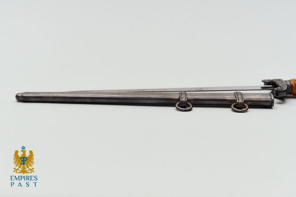 Long antique metal rod with two ring attachments and a leather-wrapped end on the right, resting on a pale surface; Empires Past logo in the bottom-left corner.