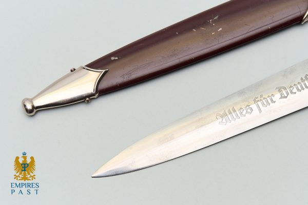Ceremonial dagger with a dark wood handle and a steel blade engraved 'Alles für Deutschland' on a pale background. Empire's Past logo in corner.