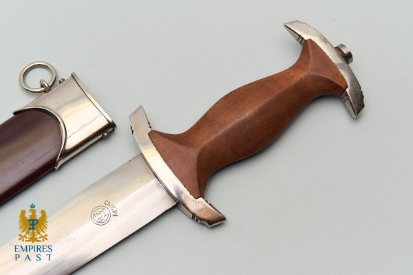 Dagger with a brown ergonomic handle and metal guard, blade partially visible, beside its sheath on a pale background; Empires Past logo bottom-left.
