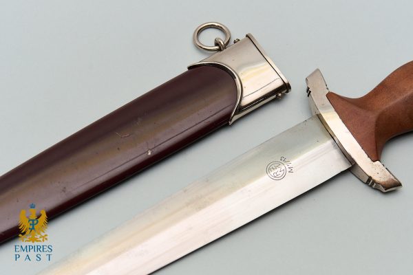 Antique dagger with a brown wooden grip and metal guard beside its brown scabbard on a pale surface.
