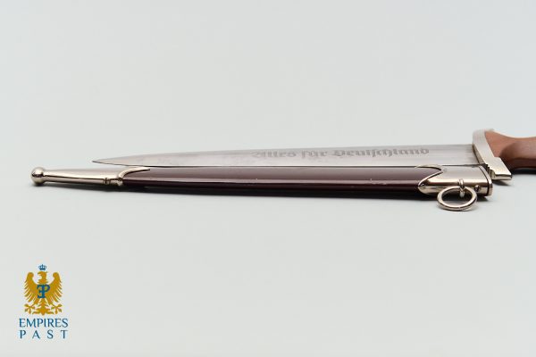 Ceremonial sword with a wooden handle and engraved blade resting on a pale surface, Empire Past watermark in the bottom-left corner.