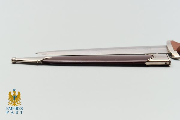 Side view of a ceremonial dagger with a brown wooden grip and silver fittings on a pale background, Empire Past logo bottom left.