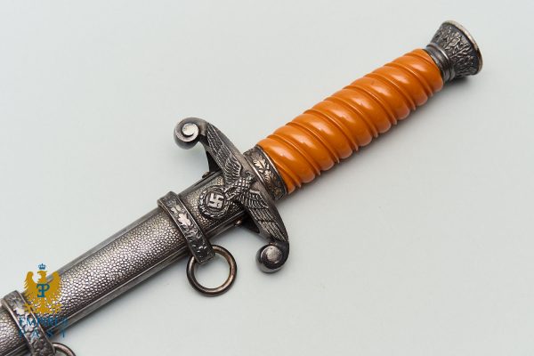 Dagger with an orange ribbed grip and ornate metal guard featuring an eagle motif, resting on a light background.