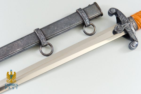Antique dagger with orange grip and ornate guard lying beside a textured metal scabbard on a pale surface, Empires Past logo bottom left.