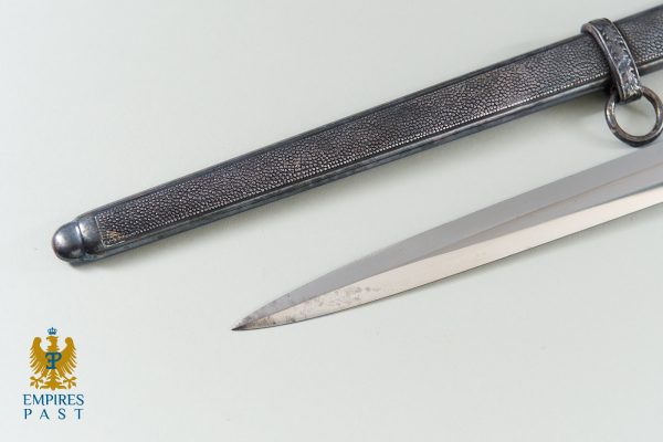 Antique dagger with a curved blade laid beside a textured scabbard on a pale surface, with the Empires Past logo in the lower-left corner.