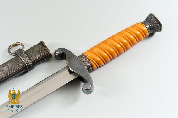 Antique dagger with an orange ribbed grip and ornate metal guard, shown next to a textured sheath on a pale background.