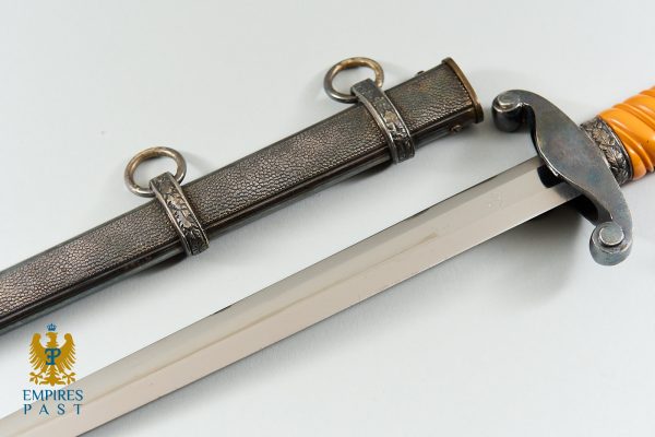 Close-up of a decorative sword with an orange grip and curved guard, laid on a pale surface; Empire's Past logo in the lower-left corner.