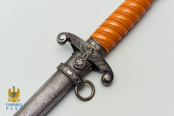 Decorative dagger with an orange ribbed grip and a metal guard featuring an eagle and swastika emblem; textured scabbard visible.