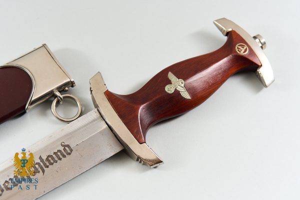Close-up of a decorative dagger with a dark wooden handle and silver metal fittings, featuring an antique imperial eagle emblem on the grip and blade edge.