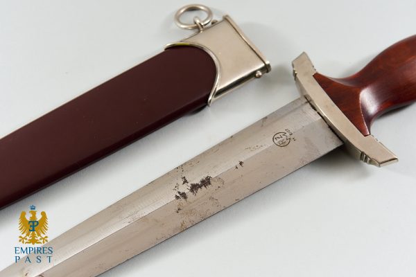 Dagger with wooden handle and metal guard next to a brown sheath on a light surface; Empire PAST watermark bottom-left.