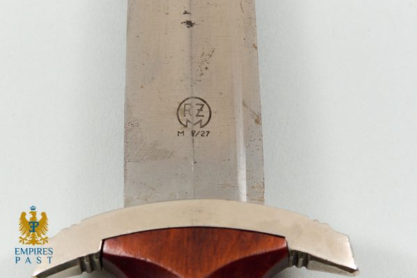 Close-up of a weathered sword blade with a circled 'RZ' maker mark and 'M 3/27' beneath, wood hilt visible at bottom left.