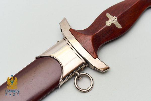Close-up of a wooden-handle dagger with silver guard, bearing a Nazi eagle and swastika insignia on the grip area in a historical artifact image.