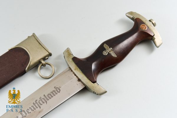 Dagger with brown wooden grip bearing a Nazi eagle emblem and a silver crossguard, blade partially exposed beside a scabbard with a ring.