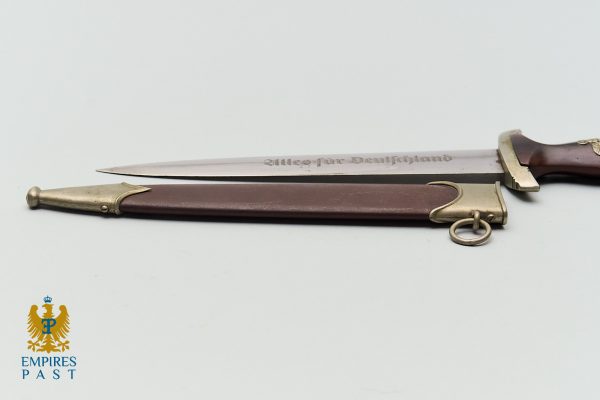 Ceremonial dagger with brown sheath and brass fittings on a white background; blade engraved 'Alles fuer Deutschland'