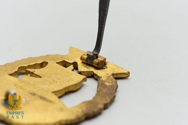 Close-up of a hammer striking a gold-colored metal emblem with cut-out shapes.