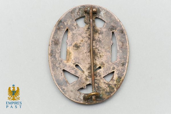 Rear view of an antique, rusted oval metal badge with a central pin.