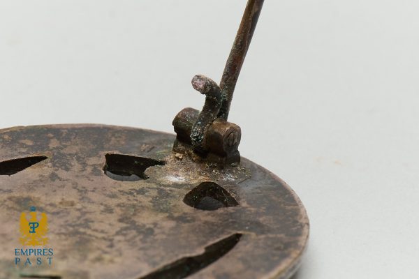 Close-up of a corroded iron key-like rod attached to a rusted circular disk with slotted openings, an antique mechanism.