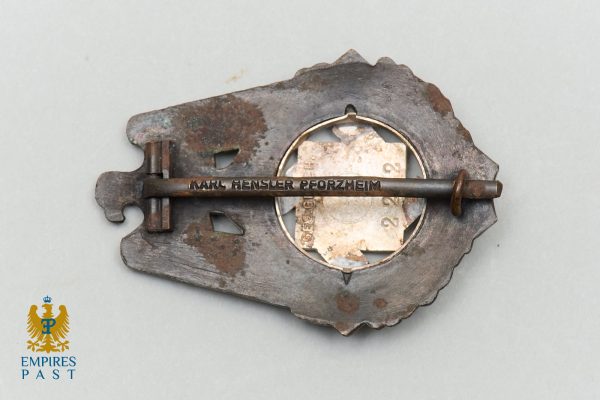 Rusty metal badge with a long horizontal pin across a circular centerpiece; appears aged and corroded, with the Empires Past logo visible in the bottom-left corner.