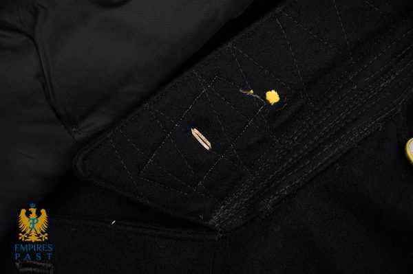 Close-up of a dark wool coat pocket with a small yellow lint/crumb and a tiny brown leaf on the fabric edge.