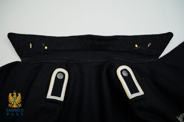 Close-up of a black military coat collar with decorative shoulder boards and gold trim.