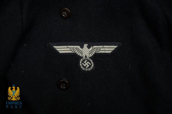 Close-up of a dark wool coat featuring a gray Nazi eagle insignia with a swastika badge in the center, near brown buttons; Empires Past logo in the bottom-left corner.