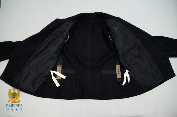 Open black coat laid flat, showing inner lining, beige adjustable waist straps, and white fabric ties on both sides.