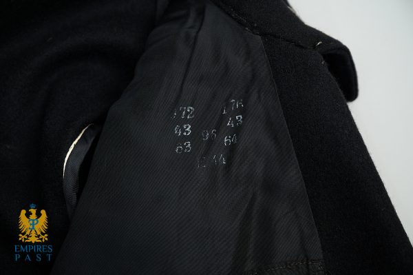 Close-up of a black coat sleeve with white chalk markings on the inner lining and a blue-gold emblem in the corner.