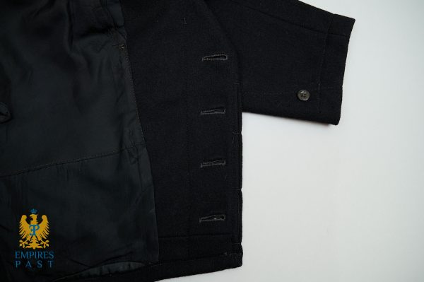 Close-up of a dark coat sleeve and inner lining with a row of buttonholes; bottom-left shows a blue and gold emblem reading 'Empires Past'.