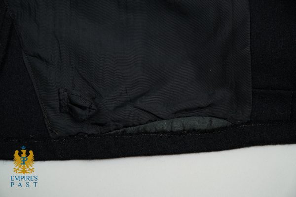 Close-up of black fabric hem and lining with a light border at the bottom, featuring the blue-and-gold Empires Past logo in the lower-left corner.