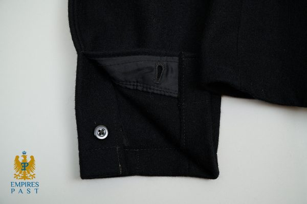 Close-up of a black wool coat sleeve cuff with a small button and stitched strap; watermark logo 'Empires Past' bottom-left.
