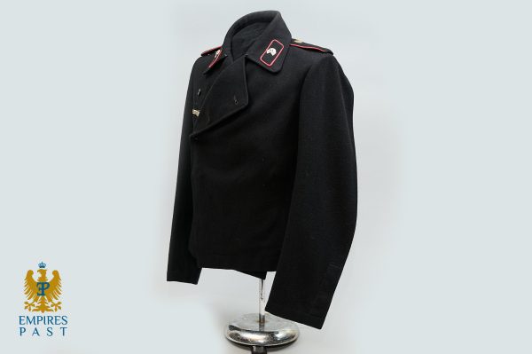 Vintage black military-style coat on a headless mannequin, with red-edged epaulettes and a double-breasted front.