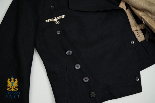 Black double-breasted military-style coat with a Nazi eagle insignia on the left chest, beige scarf tucked into the collar, and an Empire's Past logo in the bottom-left corner.