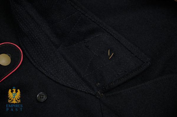 Close-up of a dark navy military-style coat with diagonal stitching, brass button, and tiny gold pins; Empires Past logo visible bottom-left.