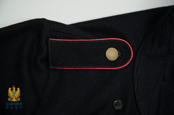 Close-up of a dark military-style jacket with red piping along a pocket flap and a brass button. Empire's Past logo visible in bottom-left.