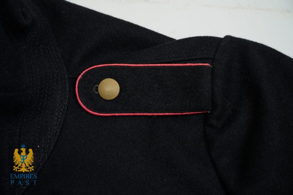Close-up of a black military-style jacket shoulder with red piping and a brass button.