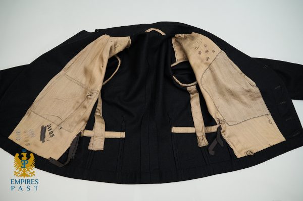 Open black coat showing beige inner lining with multiple pockets, belts, and handwritten measurements; Emprires Past logo visible in corner.