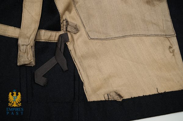 Close-up of a tan canvas pocket and strap with a dark fabric tie on a black background; Empires Past logo in the corner.