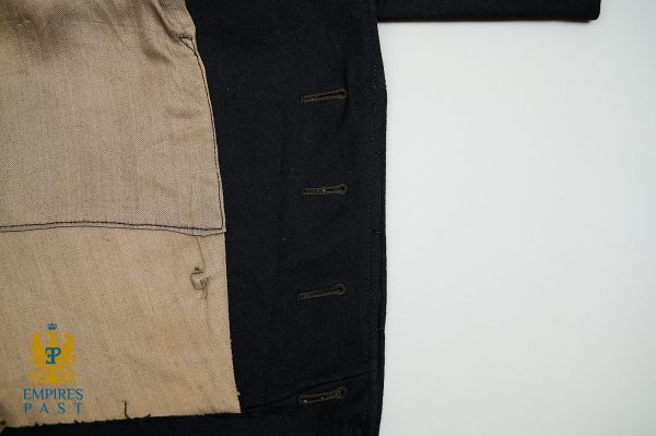 Close-up of a dark coat with brown buttonholes, showing beige lining on the left and a blue-gold emblem reading 'Empires Past' in the bottom-left corner.