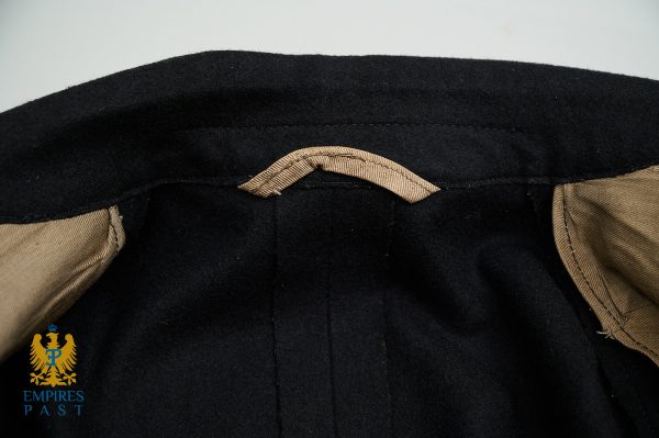 Close-up of the interior back neckline of a black coat, showing a beige fabric hanger loop and tan lining at the edges.