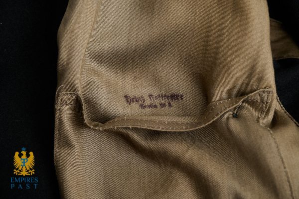 Close-up of tan fabric with a stitched hem and faint purple text, plus the Empire's Past logo in the bottom-left corner.