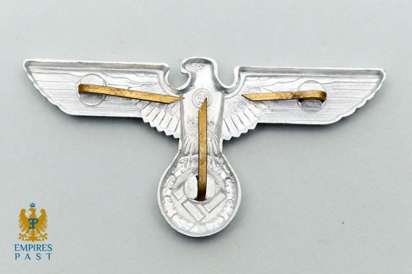 World War II-era German eagle insignia with swastika, in silver with gold pins, on a gray background.
