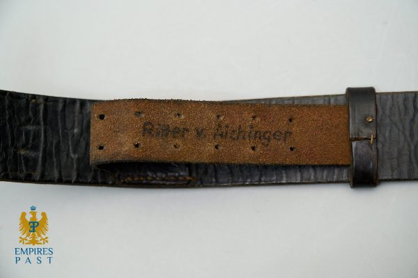 Close-up of a black leather belt with a worn brown strap showing faint brand text and rust spots, against a light background, with an Empire's Past emblem bottom left.