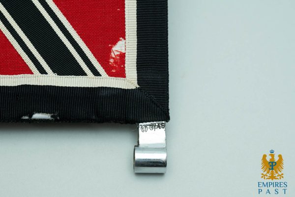 Close-up of a red, black, and white striped fabric patch with a metal clamp at the bottom edge and an Empires Past logo in the corner.