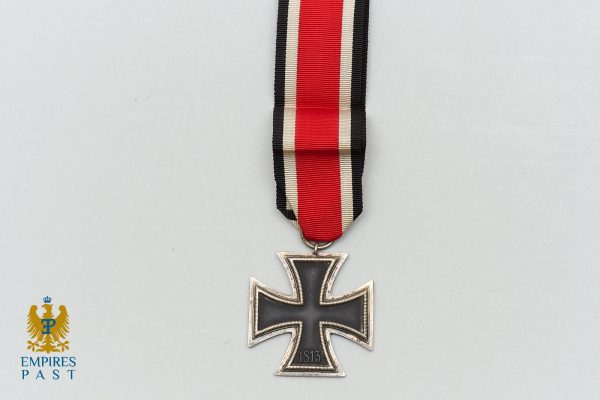 Iron Cross medal hanging from red, white, and black ribbon on a light gray background (1813) — German military decoration.