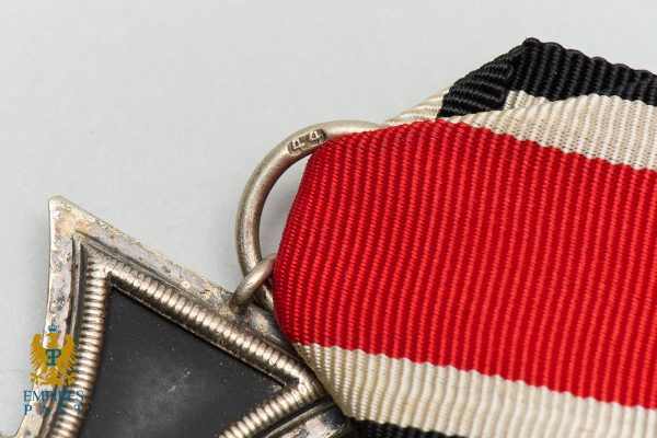 Close-up of a medal with a red and white striped ribbon threaded through a worn silver frame.