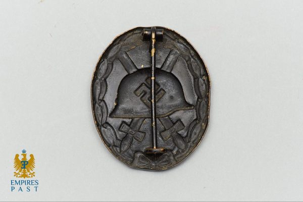 Empires Past 202517359 - Empires Past Round black metal WWII badge with a helmet centerpiece, a swastika, laurel-like border, and crossed rifles beneath; a pin runs vertically through the center.