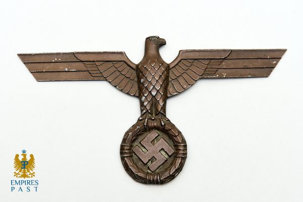Bronze eagle insignia with outstretched wings clutching a swastika inside a circular laurel-wreath.