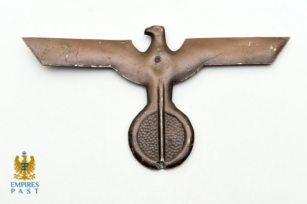 Antique hand tool with a horizontal winged blade and a central rounded grip; brown patina on pale background.