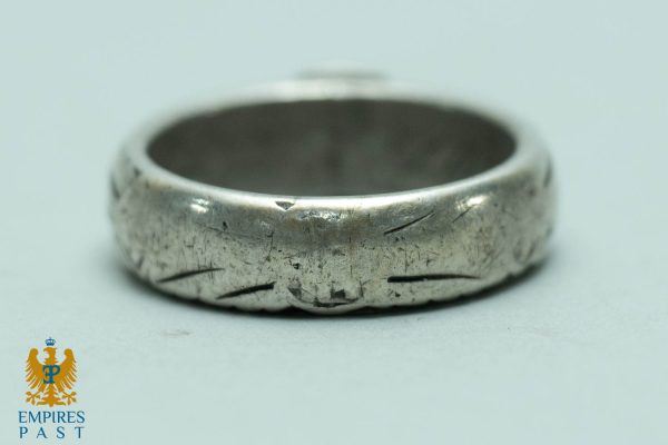 Close-up of a worn silver ring with scratches and dents on a light surface, Empires Past logo visible in the bottom-left corner.
