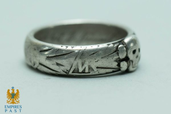 Close-up of a worn silver ring with scattered linear grooves along the band and a small round setting on the right.